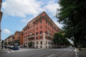 Um edifício de vários andares com fachada vermelha, uma passadeira e trilhos de elétrico.