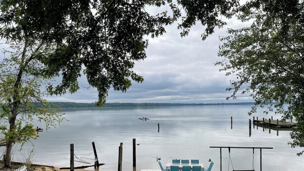 Une terrasse au bord du lac, avec une table et des chaises, une balançoire et un foyer.