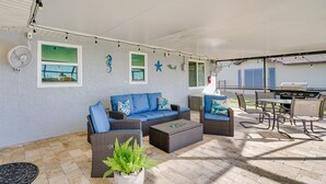 Een terras buiten met rieten meubels, een barbecue en lichtjes.