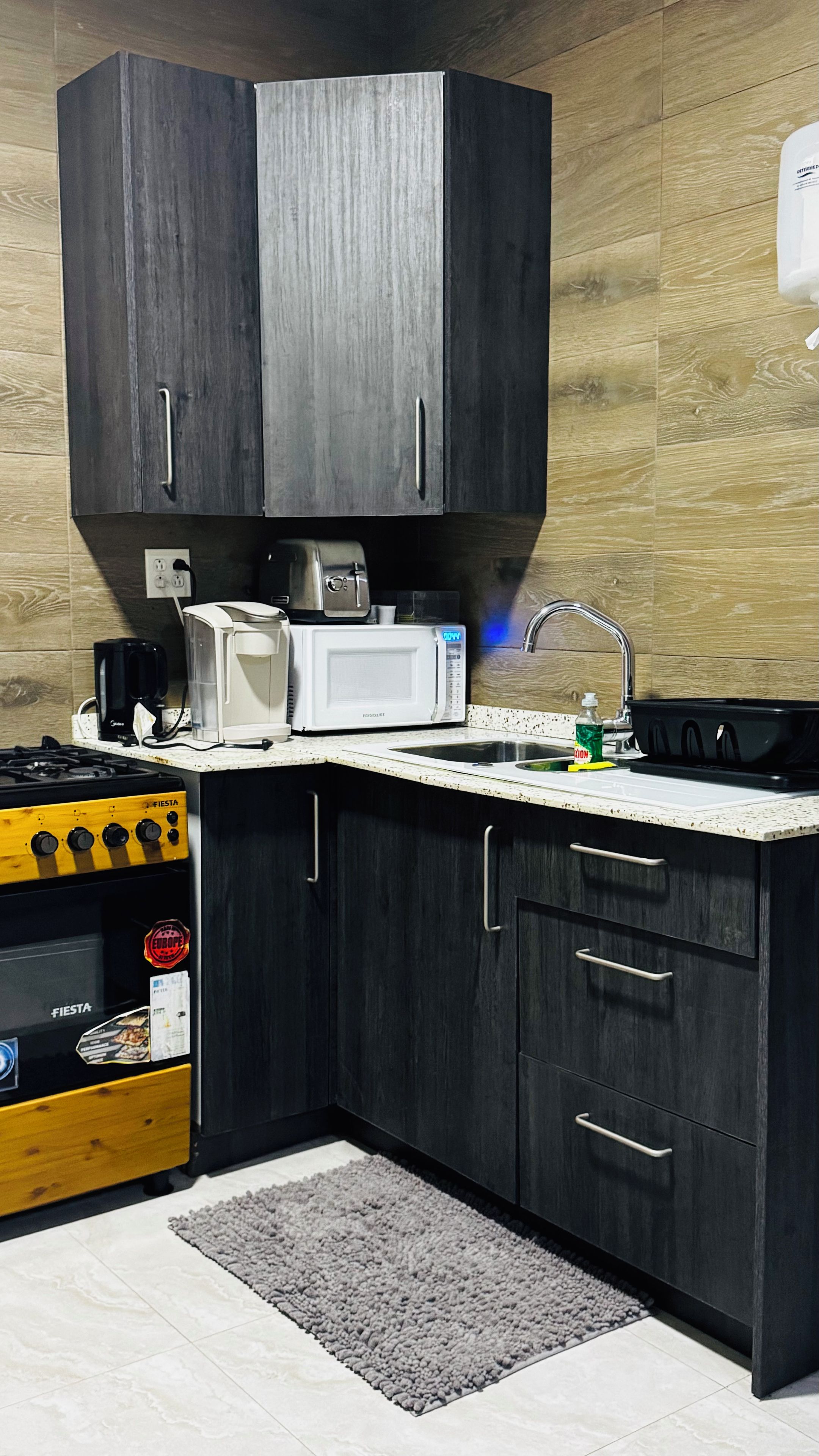 Cocina compacta con armarios oscuros, microondas, cafetera y estufa a gas.