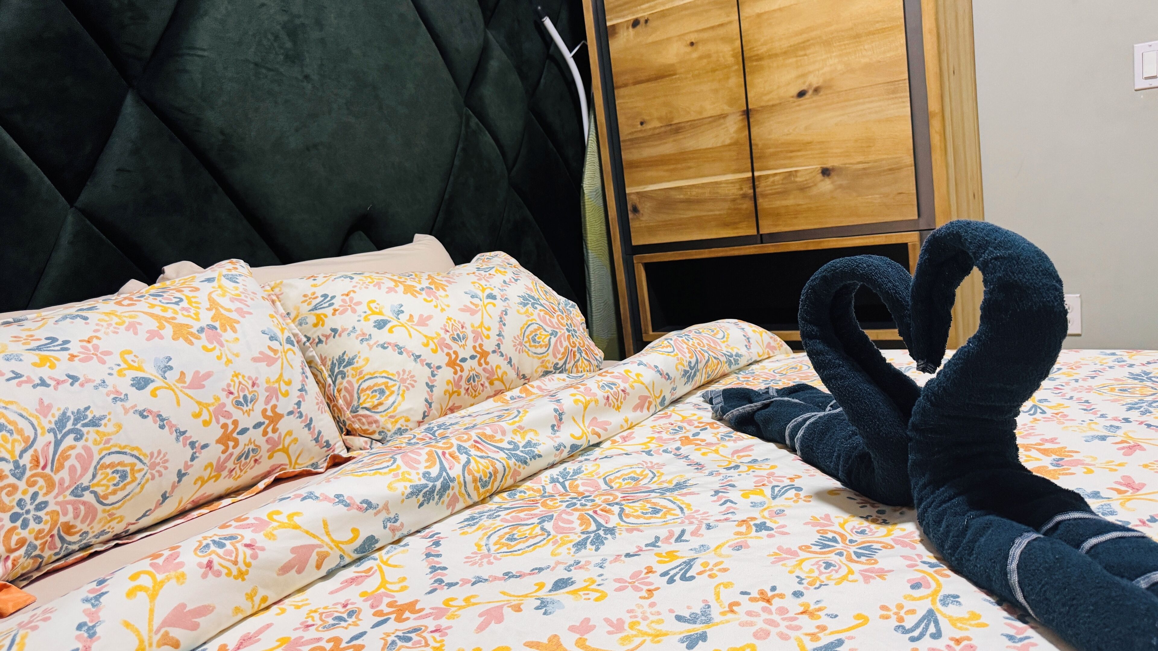 A bed with floral bedding, a black headboard, and a wooden wardrobe in the background.