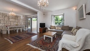 Un salon spacieux avec un mur en pierre, un lustre, un ensemble de canapés, une table basse et un téléviseur.