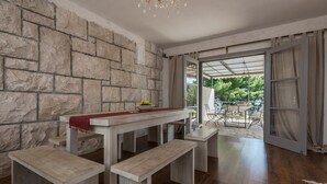 Un espace repas agrémenté d’un mur en pierre, d’une table en bois avec des bancs, et offrant une vue sur l’extérieur grâce à une porte vitrée.