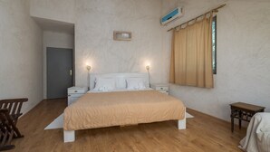 Une chambre à coucher avec un grand lit, des tables de chevet, un plancher en bois, une fenêtre avec des rideaux et un appareil de climatisation.