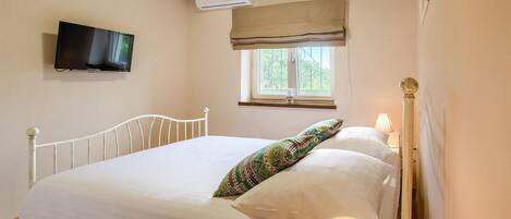 Une chambre à coucher comprenant un lit, un téléviseur fixé au mur, une fenêtre donnant sur un paysage verdoyant et une lampe de chevet.