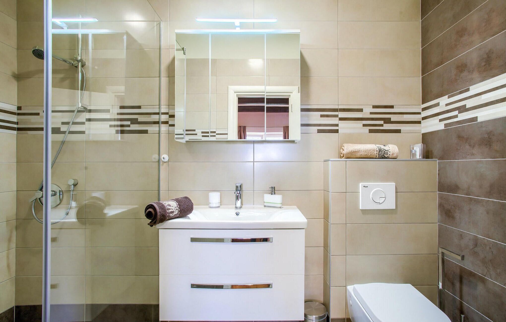 Een moderne badkamer met een glazen douchecabine, een witte wastafel met twee lades, een spiegel boven de wastafel en een handdoek aan de muur.