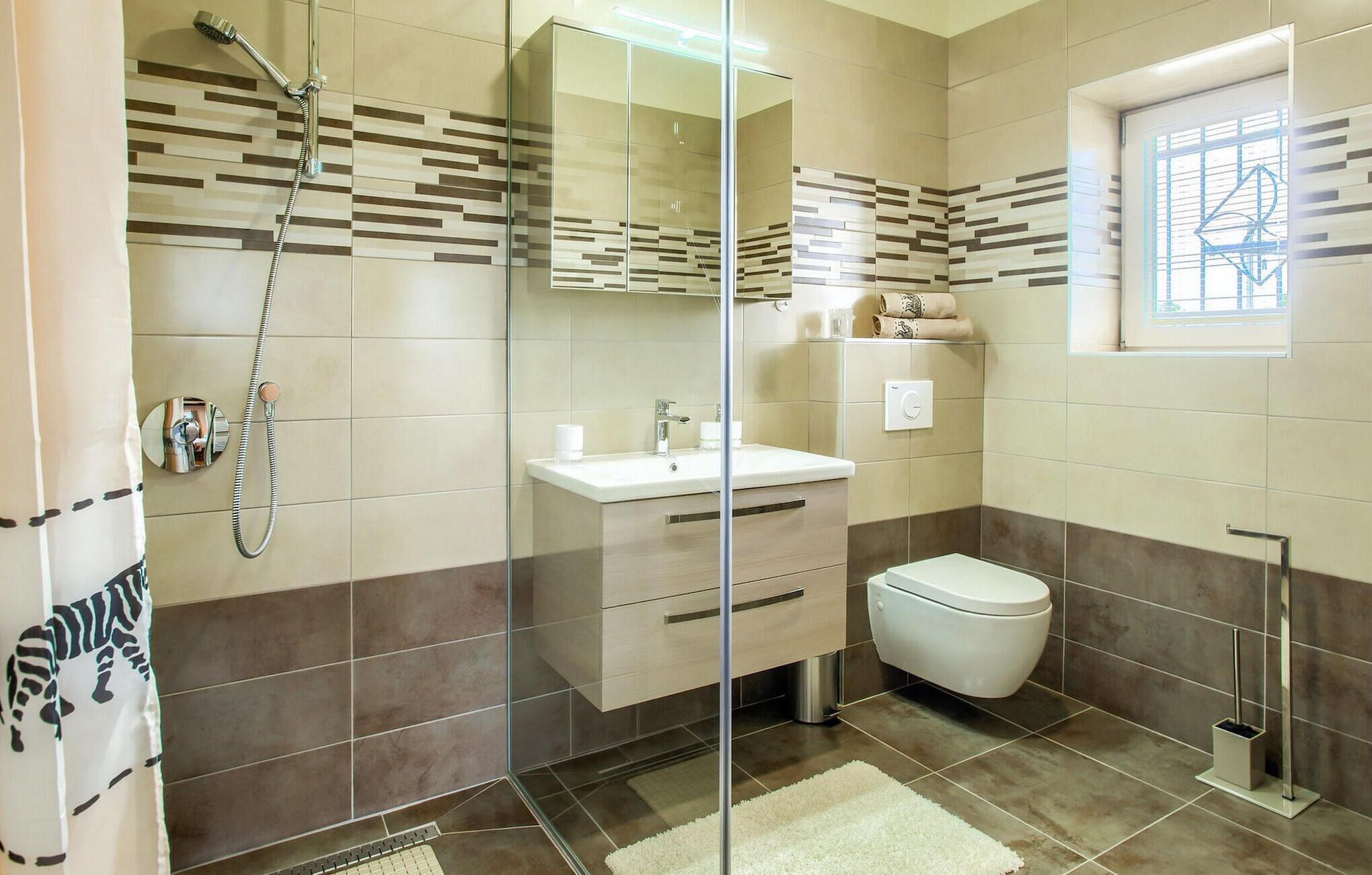 Un baño moderno con cabina de ducha de vidrio, lavabo blanco, inodoro y un ventanal con vistas.