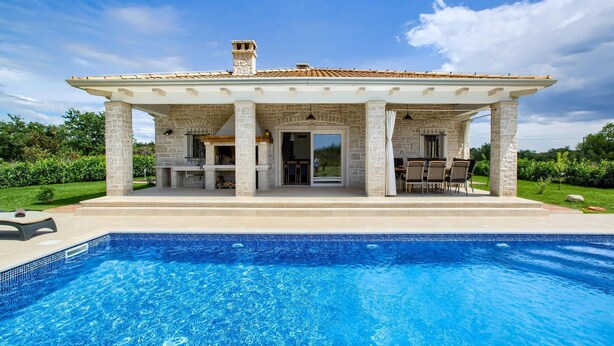 Una casa con piscina, facciata in pietra e patio coperto con mobili da esterno.