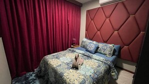 Ein Schlafzimmer mit einem Bett, roten Vorhängen, einer gemusterten Bettdecke und einem roten Kopfteil.