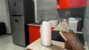 Eine Küche mit roten Schränken, einem Edelstahlkühlschrank, einer Mikrowelle und einem Sp ülbecken.