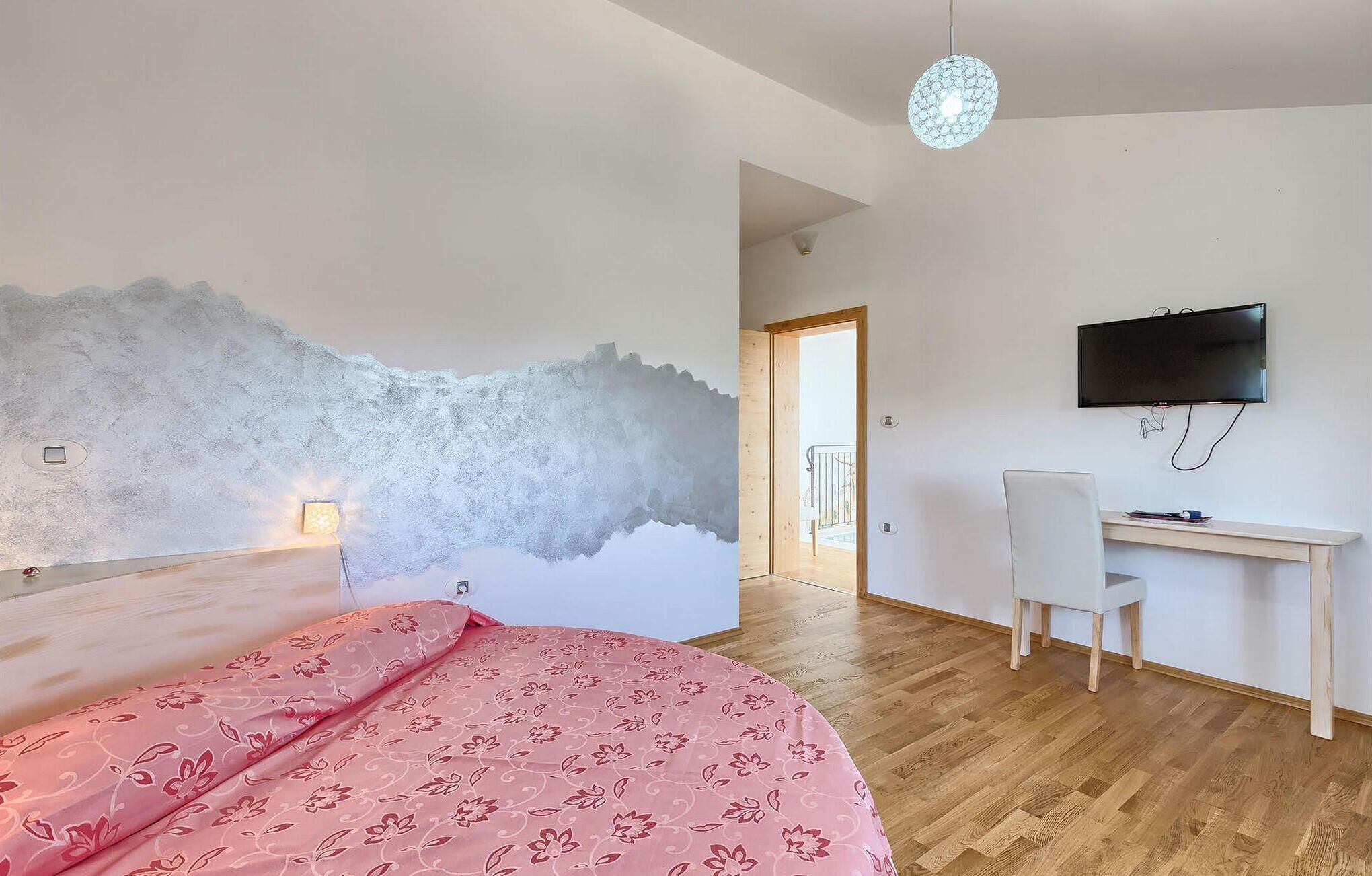 A bedroom with a bed, a desk, a chair, a television, and a wall with a textured design.