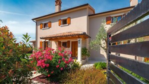 A two-story house with a tiled roof, a porch with a railing, and a garden with pink flowers. - Amazing home in Salambati (Salambati)