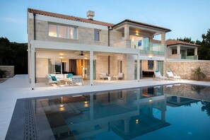 A modern two-story house with a swimming pool, outdoor seating, and a stone wall.