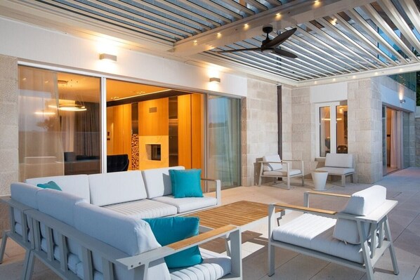 A modern outdoor living area with a white sofa, two chairs, and a wooden table.