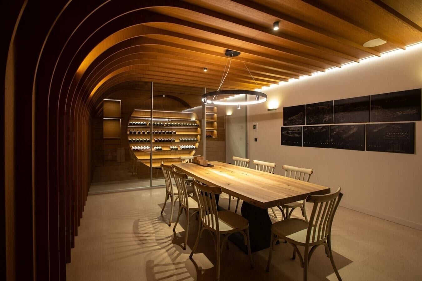 Un espace de salle à manger moderne, avec une longue table en bois et des chaises, un meuble à vin et des œuvres d’art accrochées au mur.