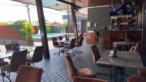 A bar area with seating, a pool, and a TV screen. - Queen's Two Bedroom Apartment (Paramaribo)