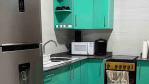 A compact kitchen with teal cabinets, a stainless steel refrigerator, a microwave, a stove, and a water dispenser. - Queen's Two Bedroom Apartment (Paramaribo)