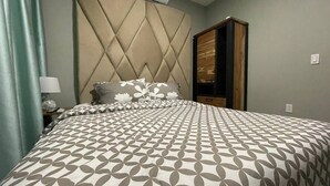 A bedroom with a bed, a headboard, a wardrobe, and a nightstand. - Queen's Two Bedroom Apartment (Paramaribo)