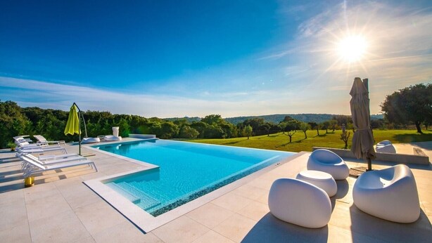 Una piscina con sillones de descanso y una sombrilla, rodeada de un jardín ajardinado y vistas al campo.