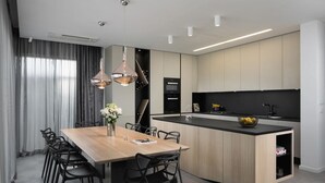 Una cocina moderna con una isla central, iluminación colgante y un comedor con mesa y sillas de madera.