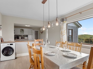 Un coin repas avec une table dressée pour quatre personnes, des chaises en bois et des luminaires suspendus.