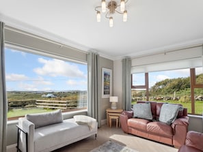 A spacious living room with a large window offering a scenic view, a leather sofa, and a white armchair.