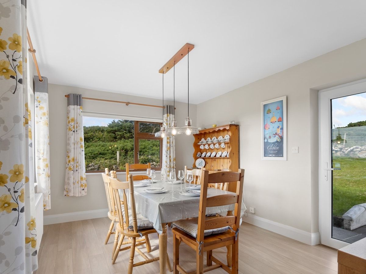 Un coin repas avec une table dressée pour quatre personnes, des chaises en bois, un luminaire suspendu et un égouttoir à vaisselle fixé au mur.