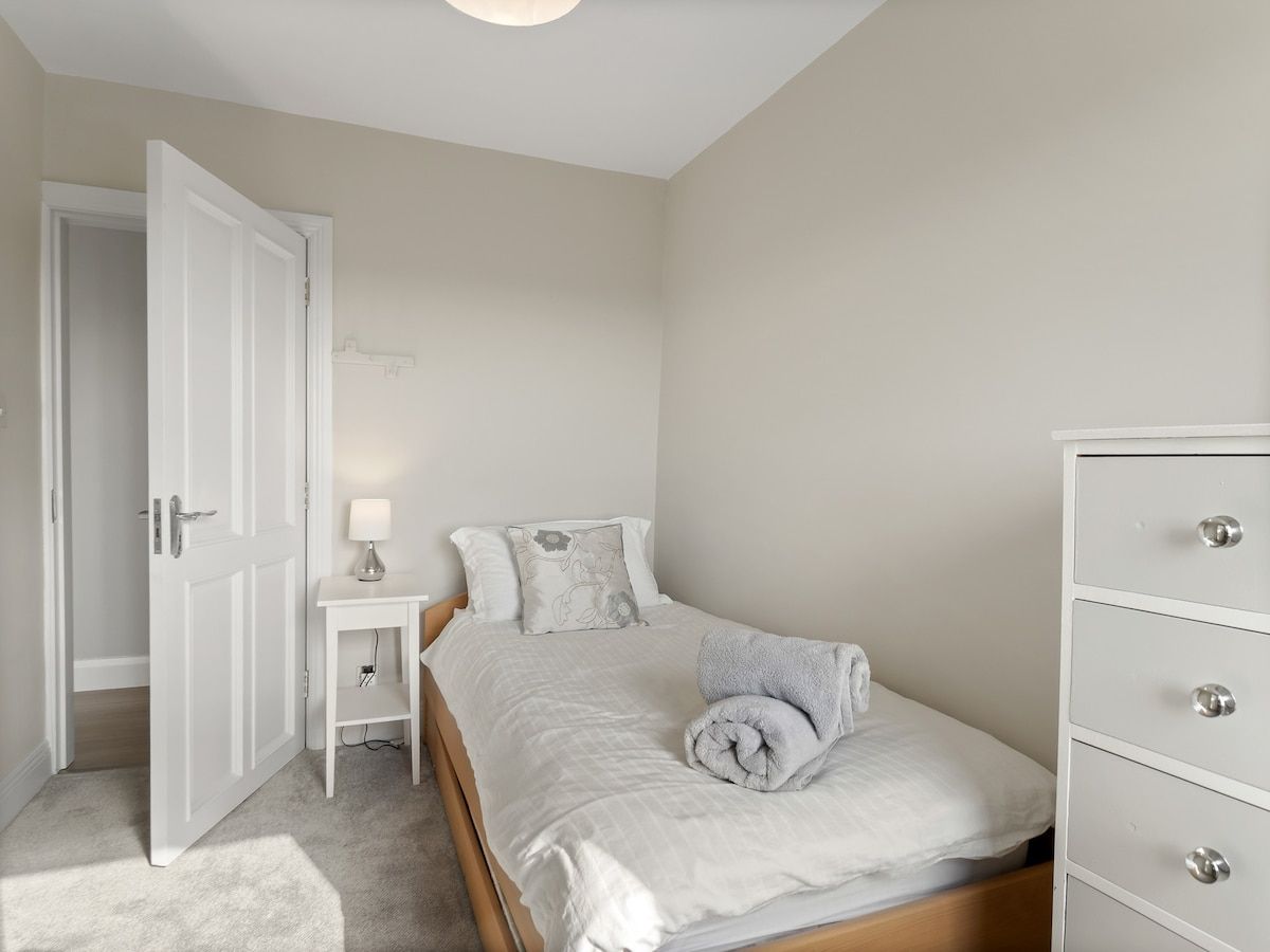 A bedroom with a bed, bedside table, lamp, and a dresser.