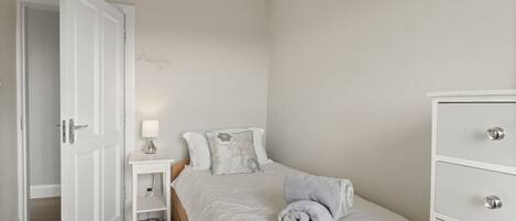 A bedroom with a bed, bedside table, lamp, and a dresser.