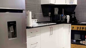 A modern kitchen with white cabinets, a stainless steel refrigerator, a coffee maker, and a stove. - Queen's Two Bedroom Apartment with Pool View (Paramaribo)