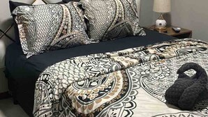 A bedroom with a tufted headboard, patterned bedding, and a bedside lamp. - Queen's Two Bedroom Apartment with Pool View (Paramaribo)