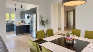 Una cocina moderna con refrigerador, microondas y lavaplatos. Hay una mesa de comedor con sillas y una planta encima.