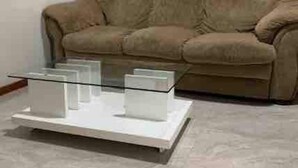 Un salon avec un canapé beige, une table basse en verre et un mur blanc.