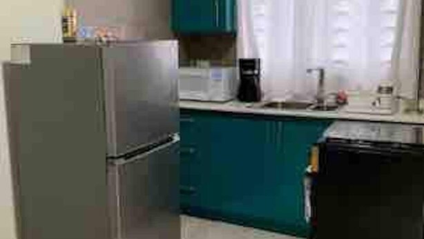 Une cuisine de taille réduite avec des meubles de couleur turquoise, un réfrigérateur, un four à micro-ondes et une machine à café.