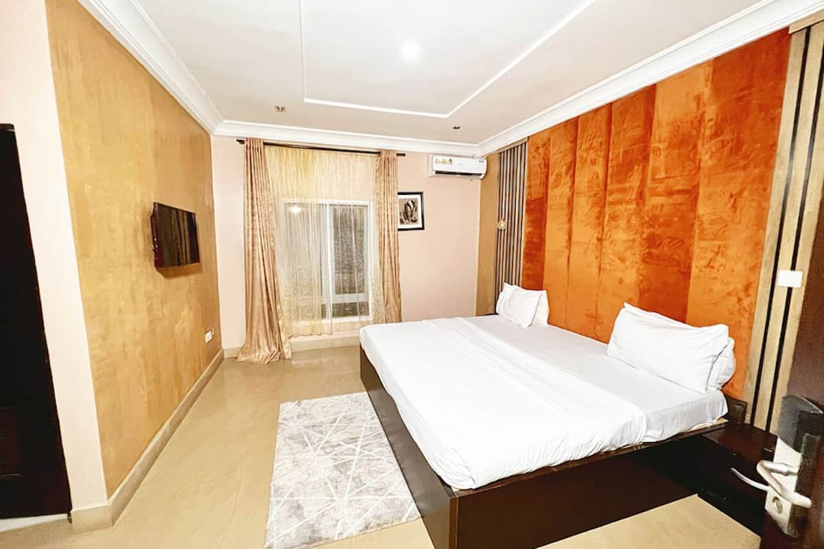 A bedroom with a large bed, a flat-screen TV, and a window with curtains.