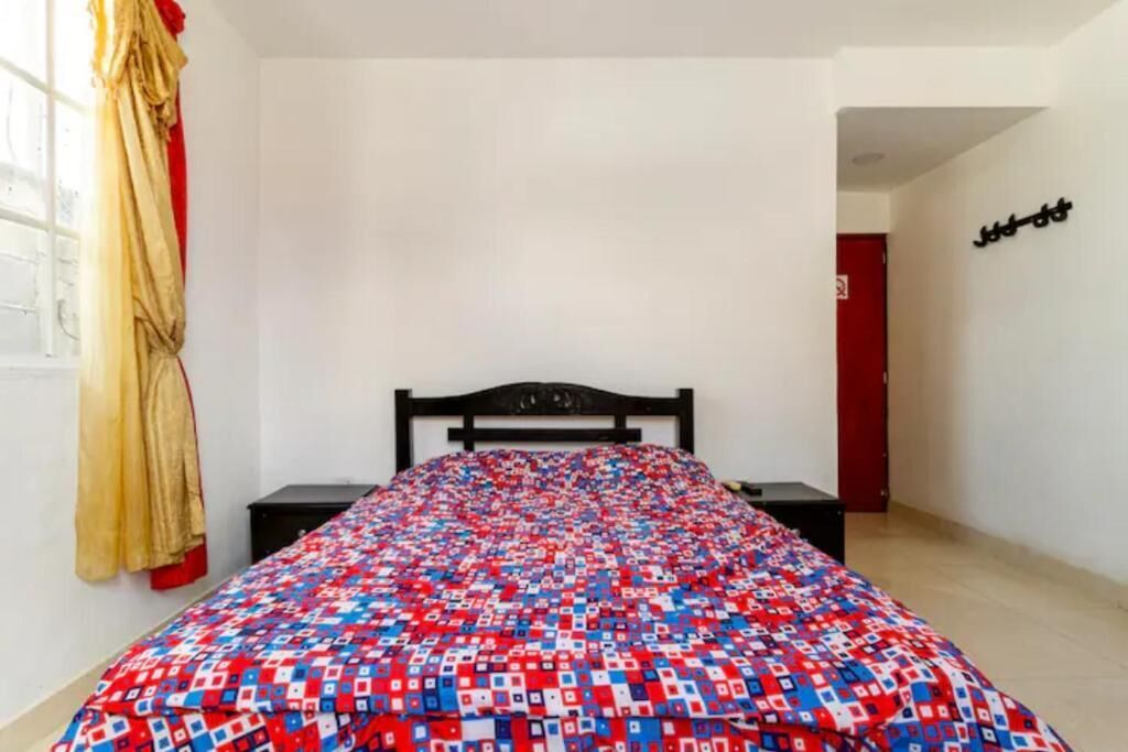 Un dormitorio con cama, mesita de noche, ventana con cortinas y puerta.