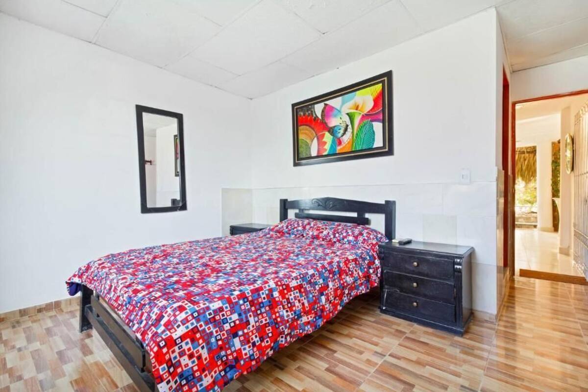 Een slaapkamer met een bed, een dressoir, een spiegel en een kleurrijk schilderij aan de muur.