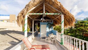 A covered outdoor seating area with a thatched roof, white railings, and a view of the beach and cityscape. - Casa Hotel Nurandy  (Cartagena)