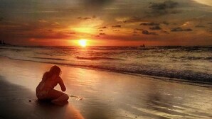 A sunset over the ocean with a silhouette of a person sitting on the beach. - Casa Hotel Nurandy  (Cartagena)