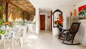 A dining area with a thatched roof, white chairs, a table with a floral tablecloth, and a rocking chair. - Casa Hotel Nurandy  (Cartagena)