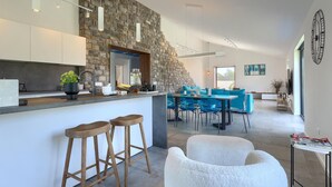A modern kitchen with a stone wall, bar stools, and a dining area with blue chairs. - Gorgeous home in Burici (Burici)