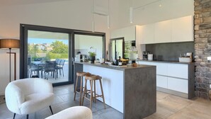 A modern kitchen with a large island, white cabinetry, and a stone accent wall. - Gorgeous home in Burici (Burici)