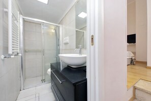 Une salle de bain avec une douche à parois de verre, un lavabo blanc et un plan de toilette noir.