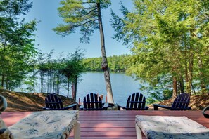 Une terrasse avec des fauteuils Adirondack donnant sur un lac, entourée d’arbres.