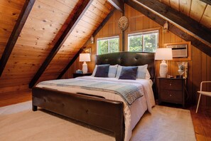 Ein Schlafzimmer mit Holzbalkendecke, einem Bett mit Kopfteil, zwei Nachttischen mit Lampen und einem Fenster.