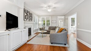 A living room with a flat-screen TV, a fireplace, a gray sofa, and a ceiling fan. - Bright Clayton Home with Screened Deck! (Clayton)