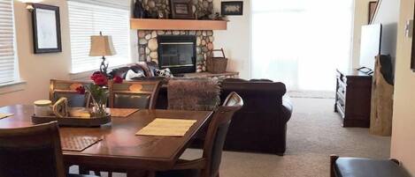 A cozy living room with a stone fireplace, a dining area with a wooden table and chairs, and a comfortable seating area with a sofa and a bench.