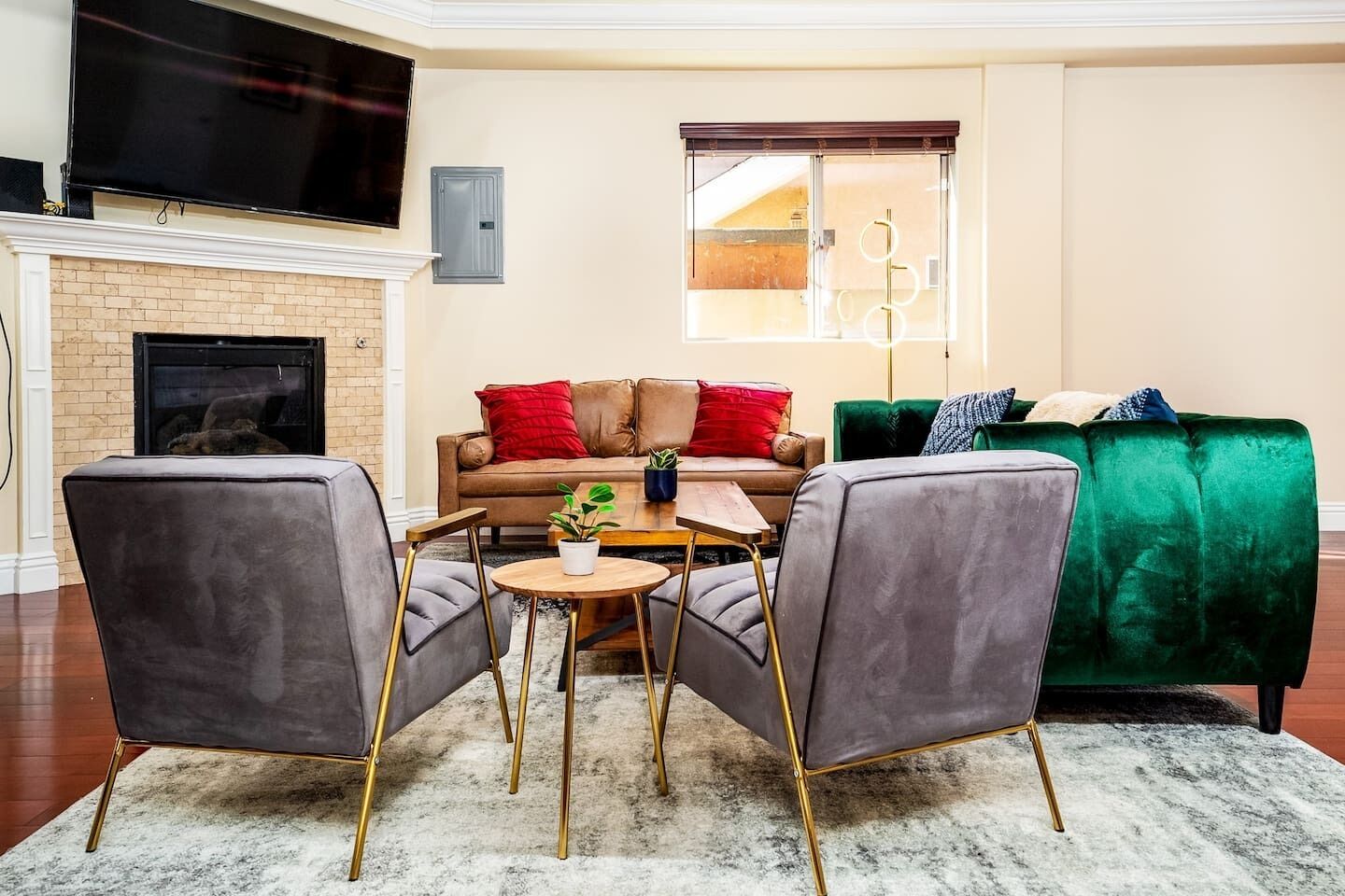 A living room with a fireplace, a green sofa, a brown sofa, and two grey armchairs.