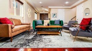Un salon comprenant un canapé en cuir marron, un canapé en velours vert, une table basse en bois et un fauteuil gris.