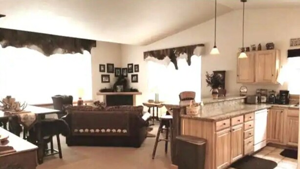 Una cocina con armarios de madera, un comedor con sofá y un taburete de bar.